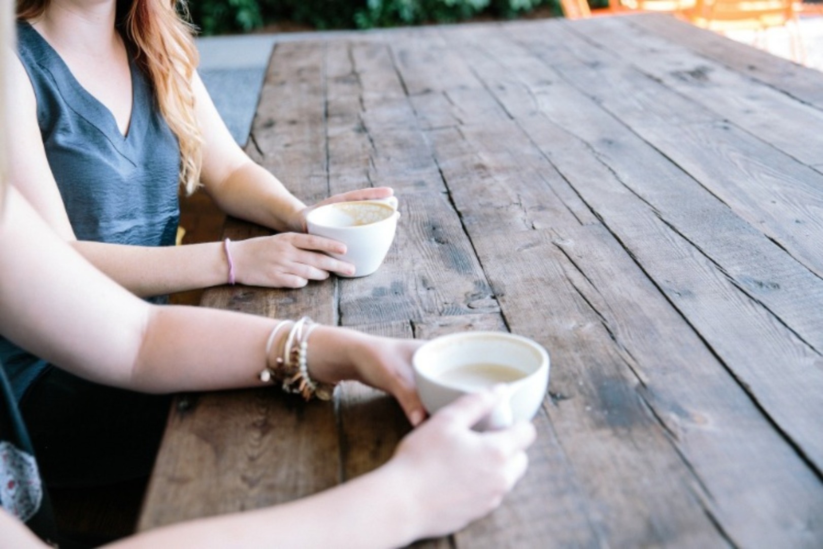 Two people sit at a wooden table chatting over tea and coffee